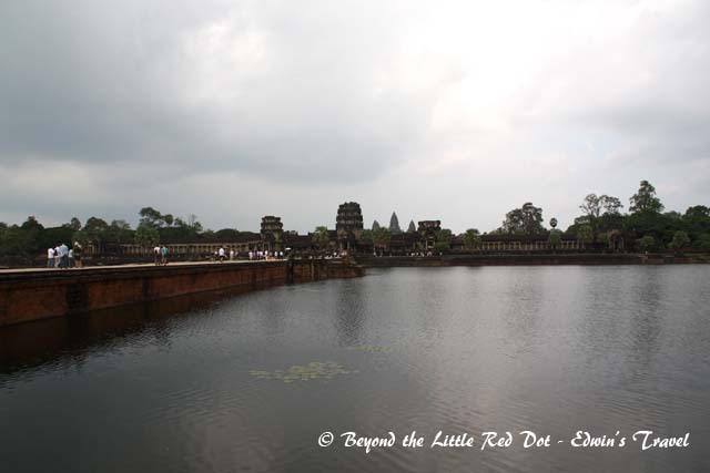 Angkor Wat is truly huge for a temple. It's surrounded by a moat and here you can see the causeway leading to the temple walls. The sky doesn't look very good with all the dark clouds.