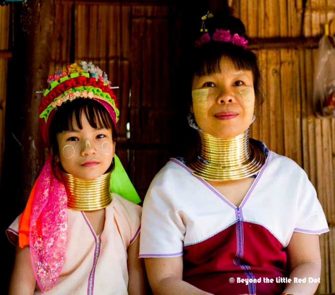 A mother and her daughter pose for a photo as they sit outside their house.